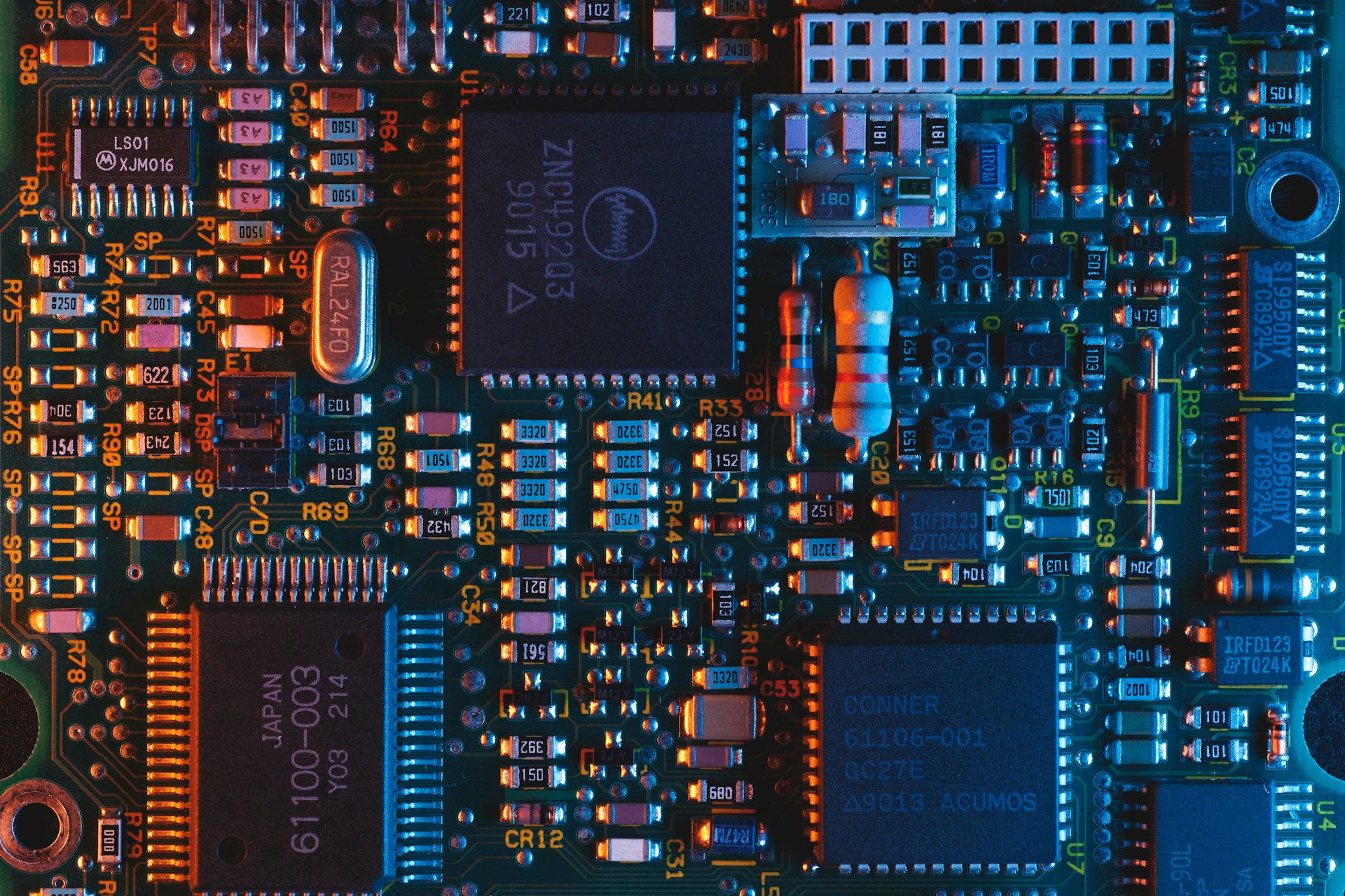 Close-up of a dense printed circuit board with integrated circuits, resistors, and capacitors.